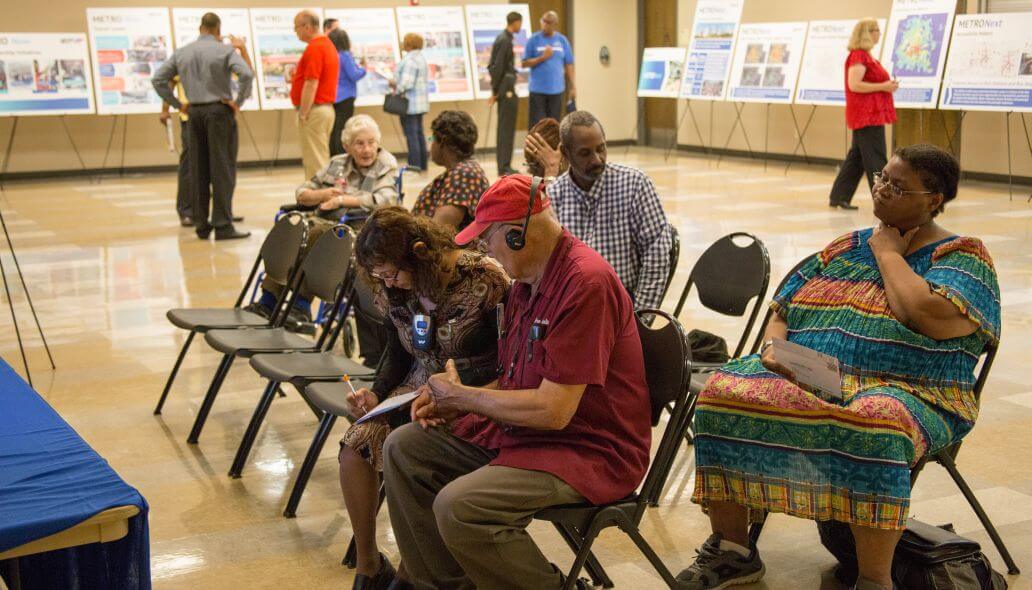 Community members sitting in foreground while others view METRONext easel signs in the background.